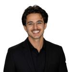 Justin Catalano, User Experience Design Lead at Leidos QTC Health Services, smiles at the camera in a professional headshot wearing a black blazer, black collared shirt, and glasses against a clean, plain background.