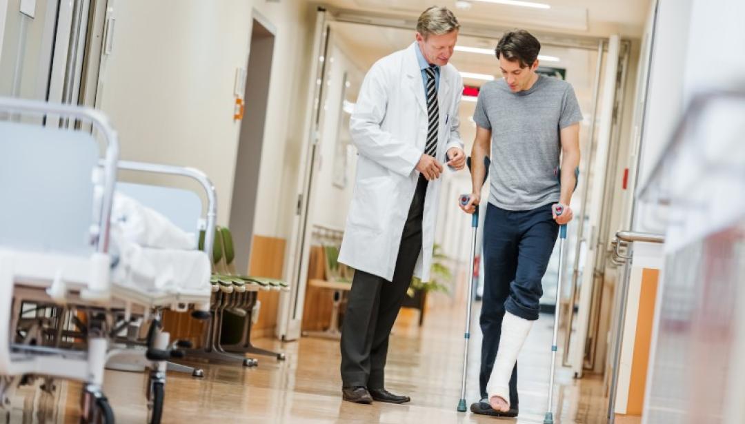 Man with broken leg talking with doctor in hospital corridor.