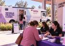 Leidos QTC Health Services mobile health clinic parked outside a community center, with visitors checking in for health screenings and others entering the clinic.
