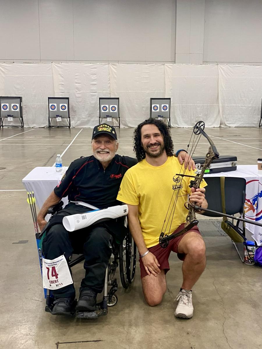 Harrison Kish (right) holding an archery bow next to an athlete. 