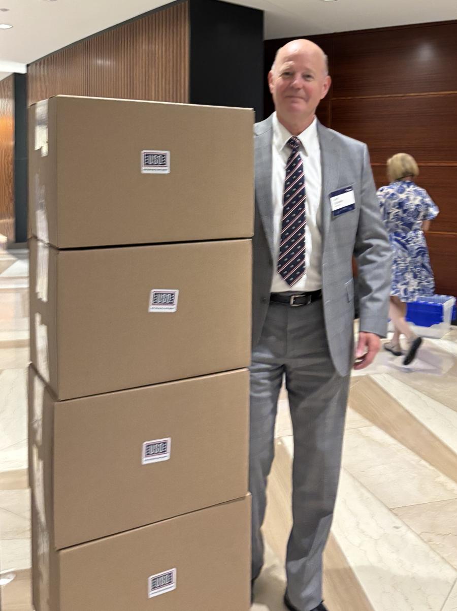 Man, wearing a suit and tie, standing next to large stack of boxes