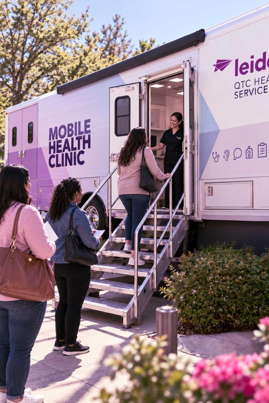 A healthcare worker welcomes a visitor into the Leidos QTC Health Services mobile health clinic as others wait near the entrance.
