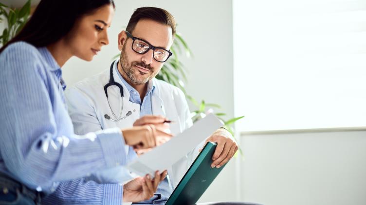 Doctor Consulting Patient and Reviewing Medical Records in a Bright Clinic 