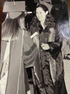 Black and white photo of woman in graduation regalia accepting her diploma