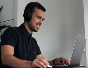 Man with headset smiling as he looks at his laptop screen